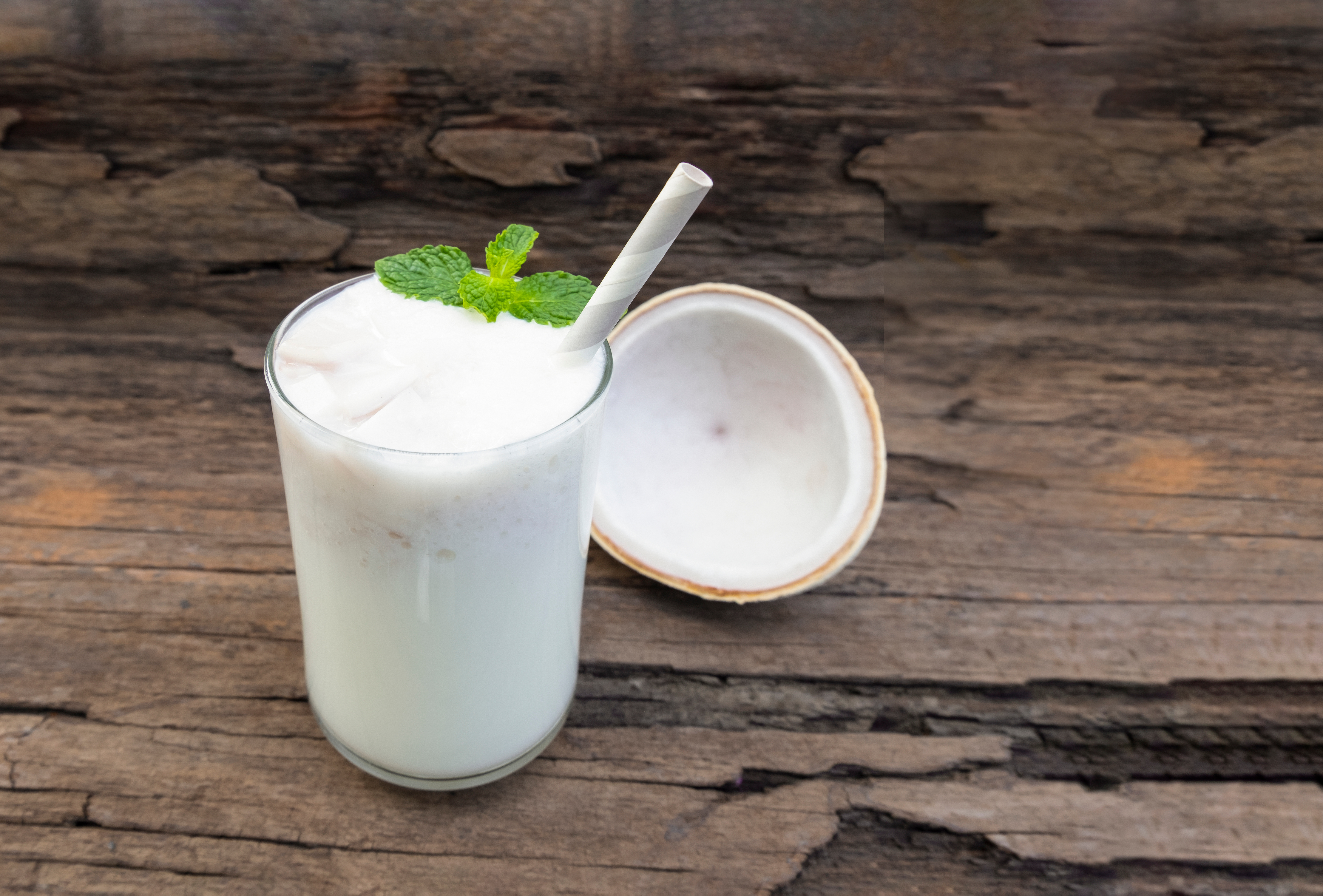 Coconut drink with mint garnish and straw on wooden table.