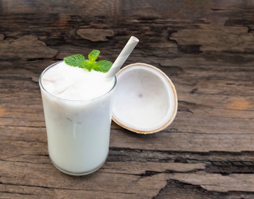 Coconut drink with mint garnish and straw on wooden table.