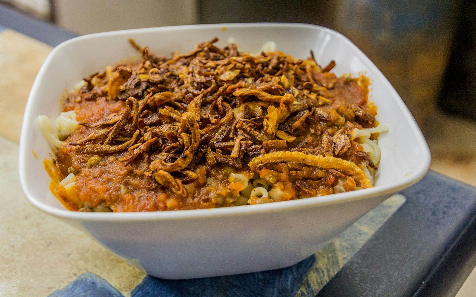 Bowl of Egyptian Koshari with lentils, pasta, rice, and crispy onions.