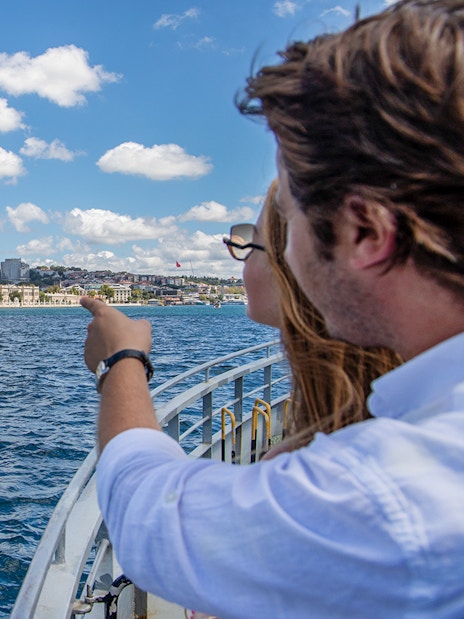 Couple on Bosphorus cruise pointing at Dolmabahçe Palace, Istanbul.