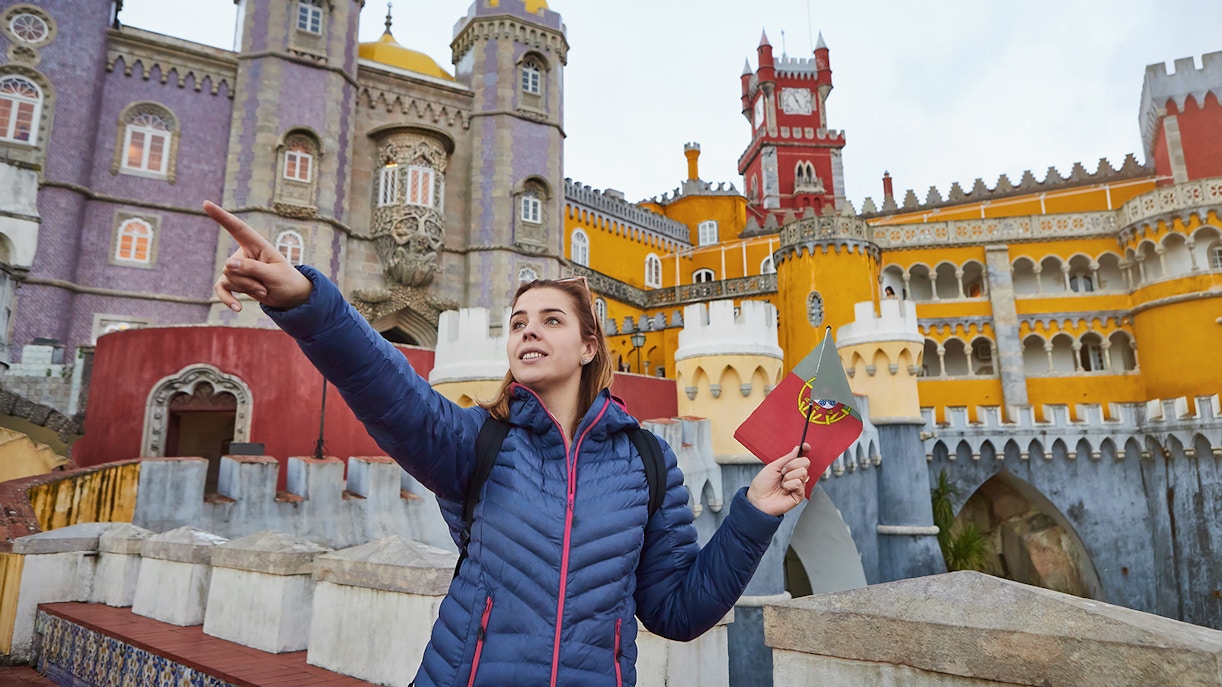 Tourist holding a Portuguese flag in front of colorful Pena Palace, Sintra.