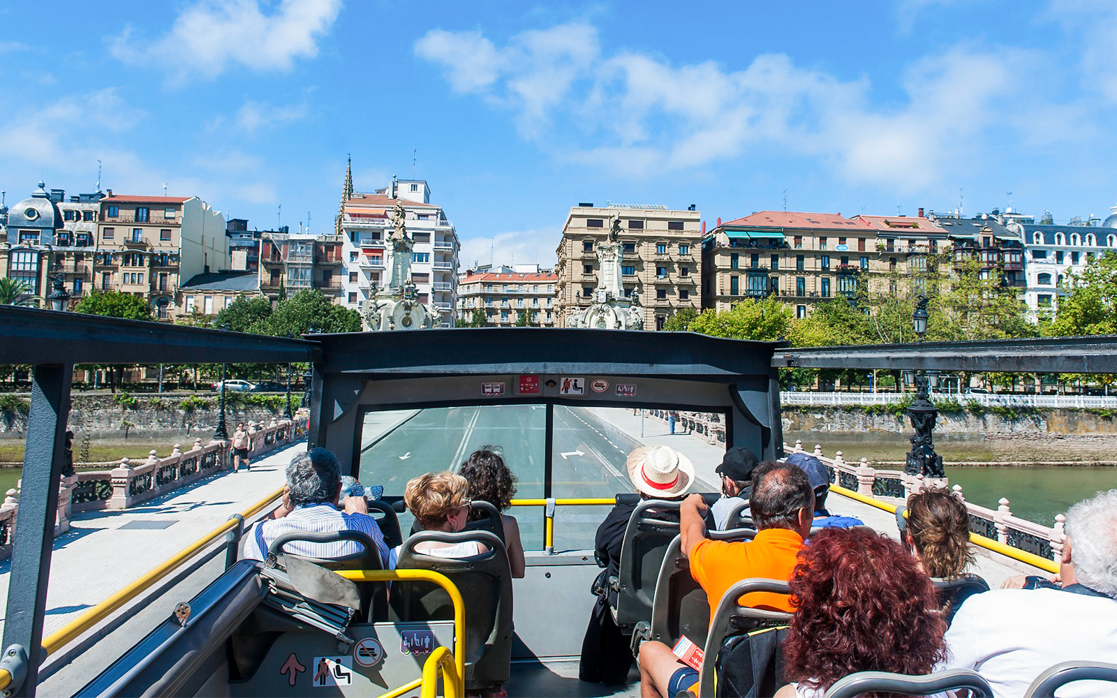 Open-top bus tour in San Sebastian city with passengers viewing historic architecture.