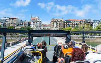 Open-top bus tour in San Sebastian city with passengers viewing historic architecture.