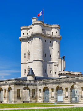 Château de Vincennes tower with French flag against blue sky.