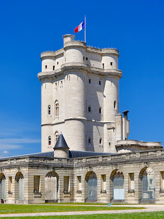 Château de Vincennes tower with French flag against blue sky.