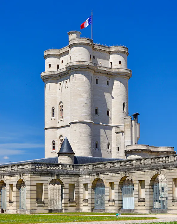 Château de Vincennes tower with French flag against blue sky.