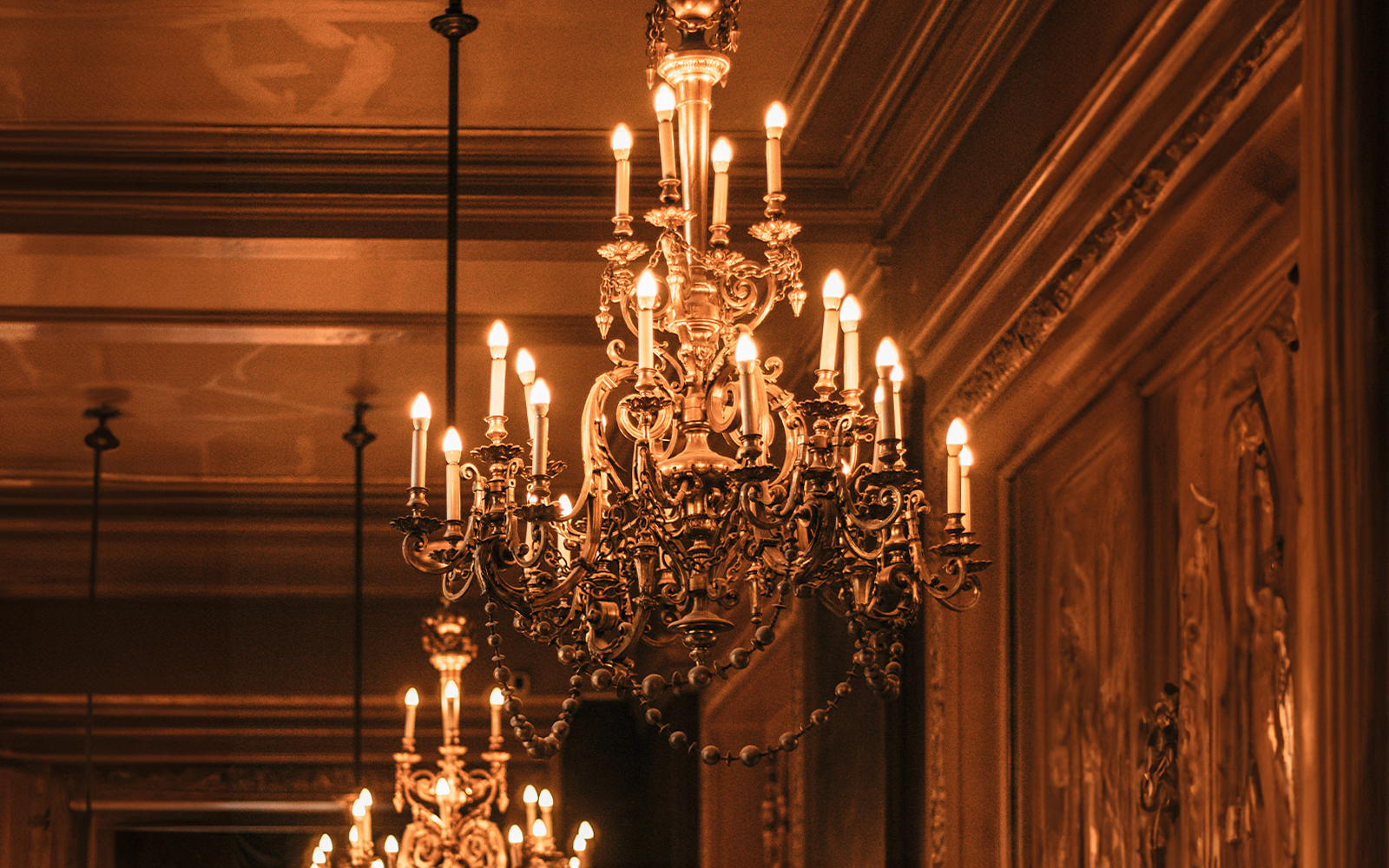 Vintage chandelier with ornate design and lit candles in an elegant room.