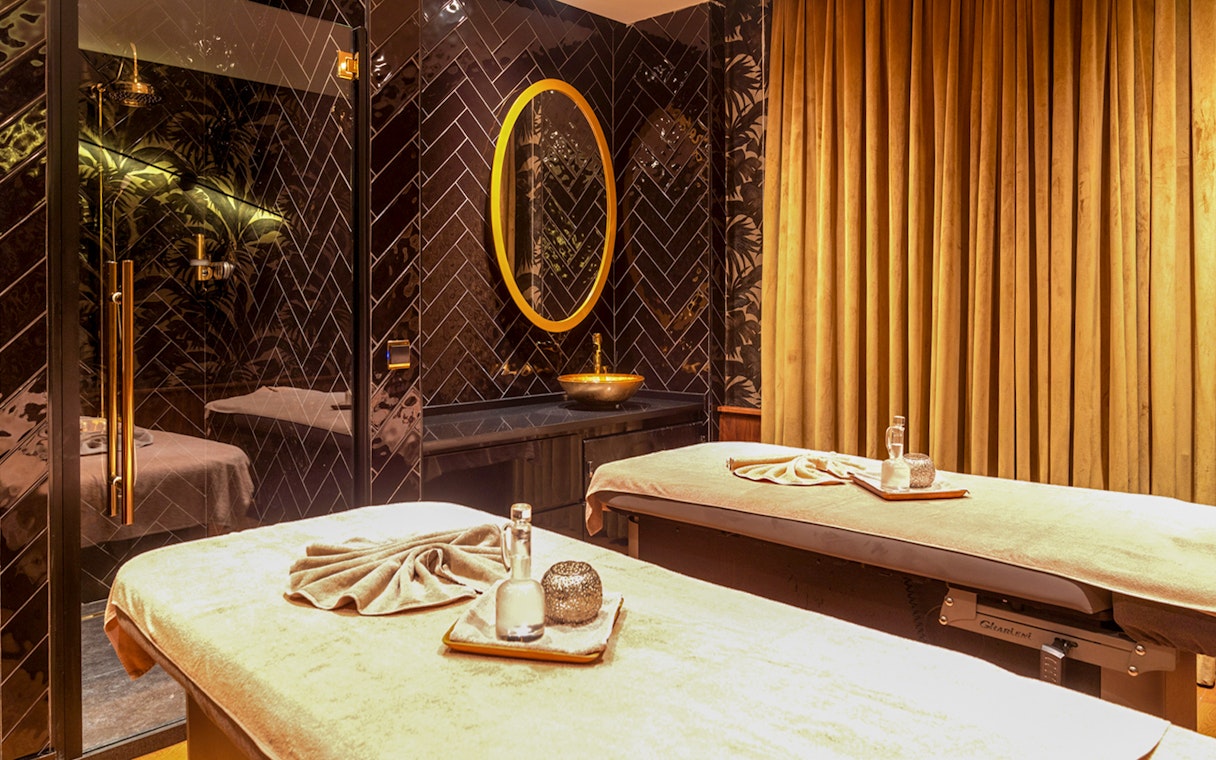 Two massage tables in a luxurious Istanbul Turkish bath with golden decor and ambient lighting.
