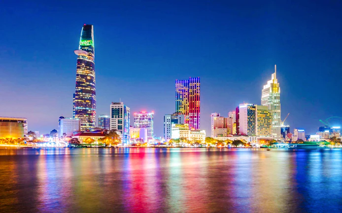Saigon cityscape at night with illuminated skyscrapers reflecting on the river.