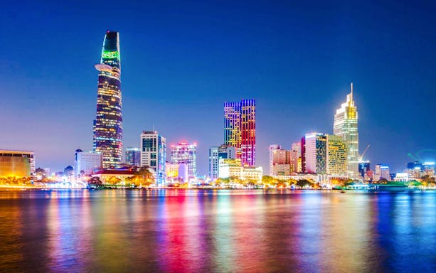 Saigon cityscape at night with illuminated skyscrapers reflecting on the river.