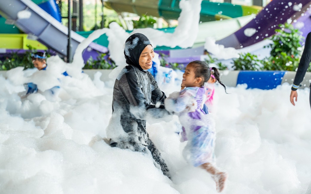 Woman and child playing in foam at a water park splash zone.
