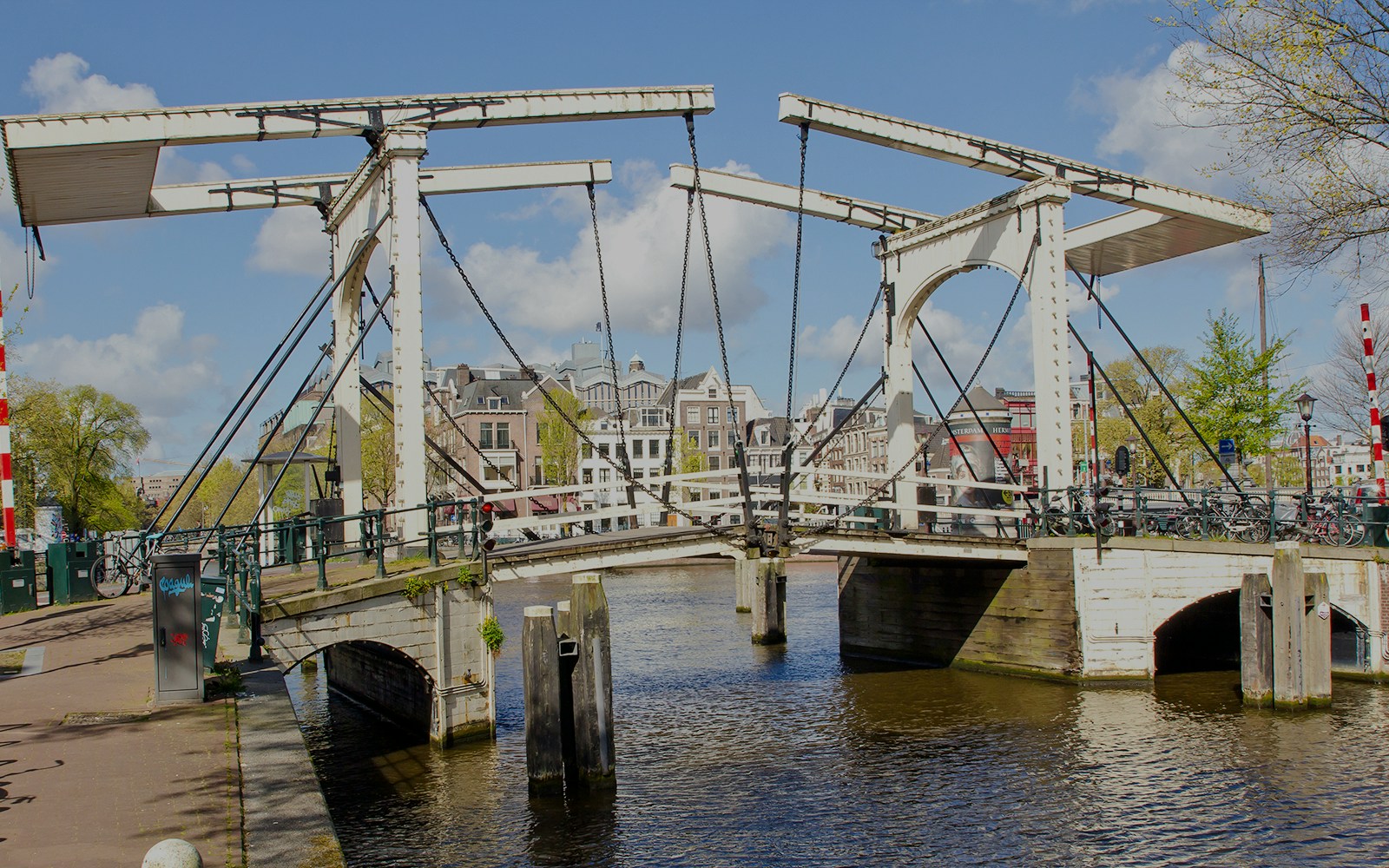 Drawbridge over Nieuwe Herengracht canal in Amsterdam with city buildings in the background.