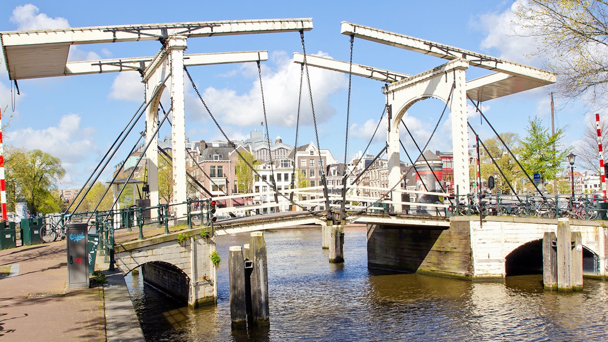 Drawbridge over Nieuwe Herengracht canal in Amsterdam with city buildings in the background.