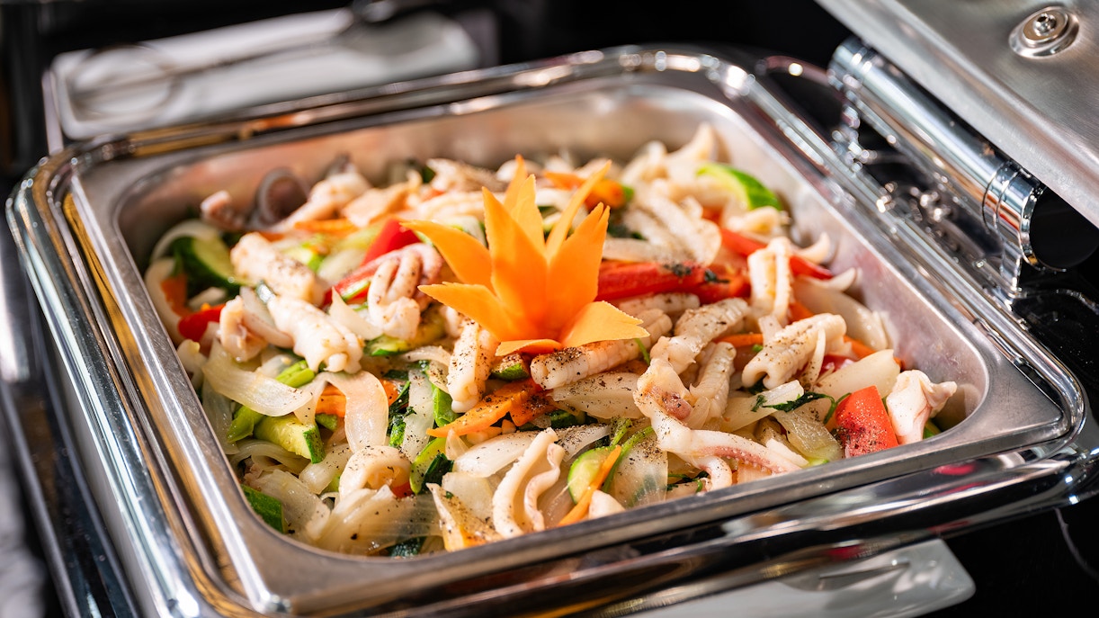 Stir-fried seafood and vegetables in chafing dish, garnished with orange flower.