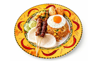 Nasi goreng with satay skewers, fried egg, and sides on a decorative plate.