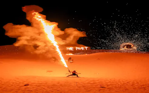 Fire performer at Dubai VIP Desert Safari with "The Fort" in flames, Dubai desert night.