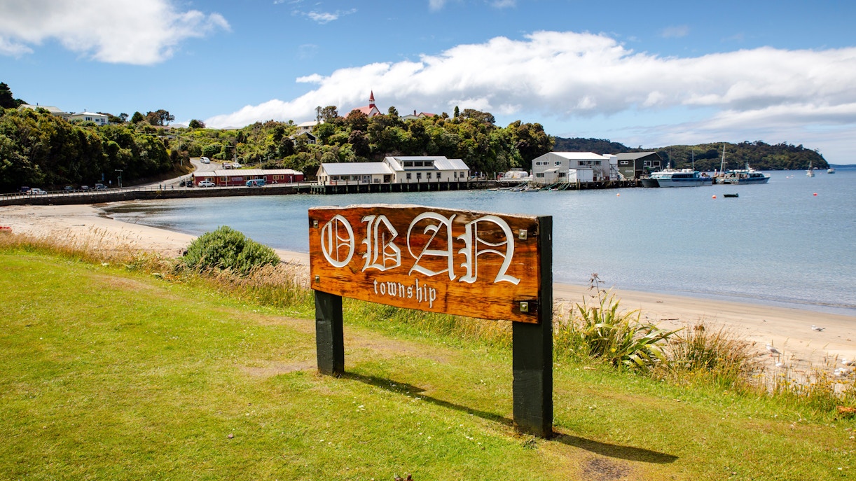 Oban town sign with waterfront view, Stewart Island, New Zealand.