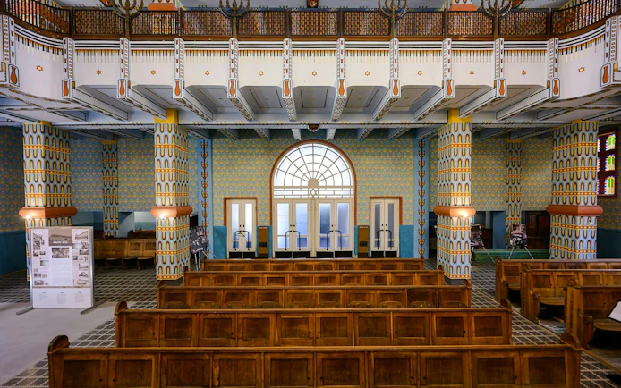 Interior view of Kazinczy Synagogue in Budapest with ornate columns and wooden pews.