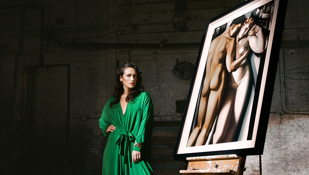 Woman in green dress standing beside a framed Lempicka painting on an easel.