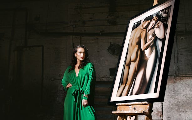 Woman in green dress standing beside a framed Lempicka painting on an easel.