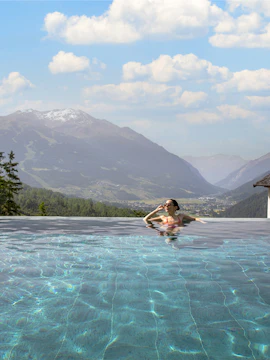 Person relaxing in an infinity pool with mountain views at QC Terme Bagni Vecchi di Bormio.