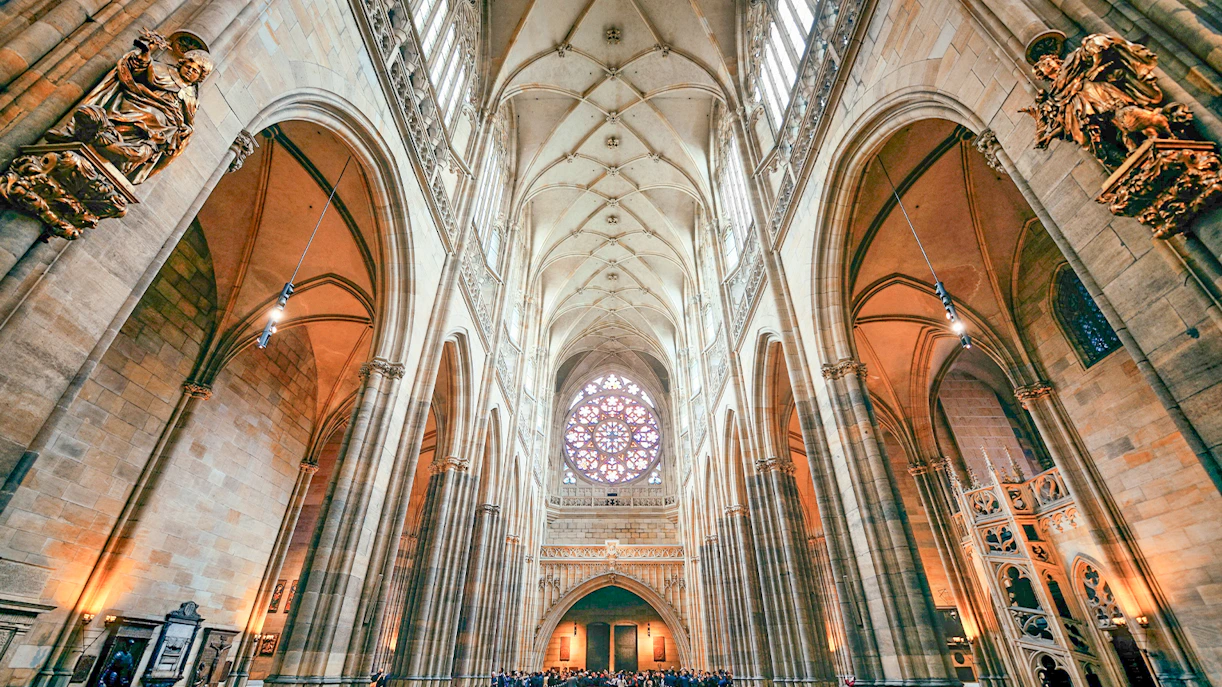 Interior of St. Vitus Cathedral with vaulted ceilings and stained glass window.