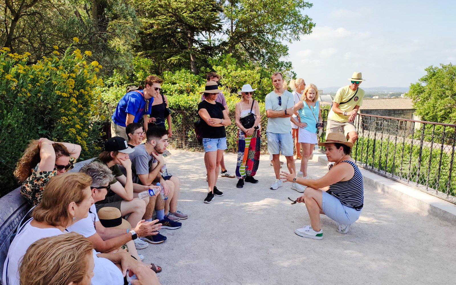 Tour group listening to a guide at Rocher des Doms in Avignon, surrounded by greenery.