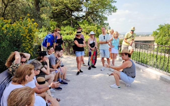 Tour group listening to a guide at Rocher des Doms in Avignon, surrounded by greenery.