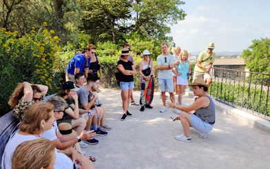 Tour group listening to a guide at Rocher des Doms in Avignon, surrounded by greenery.