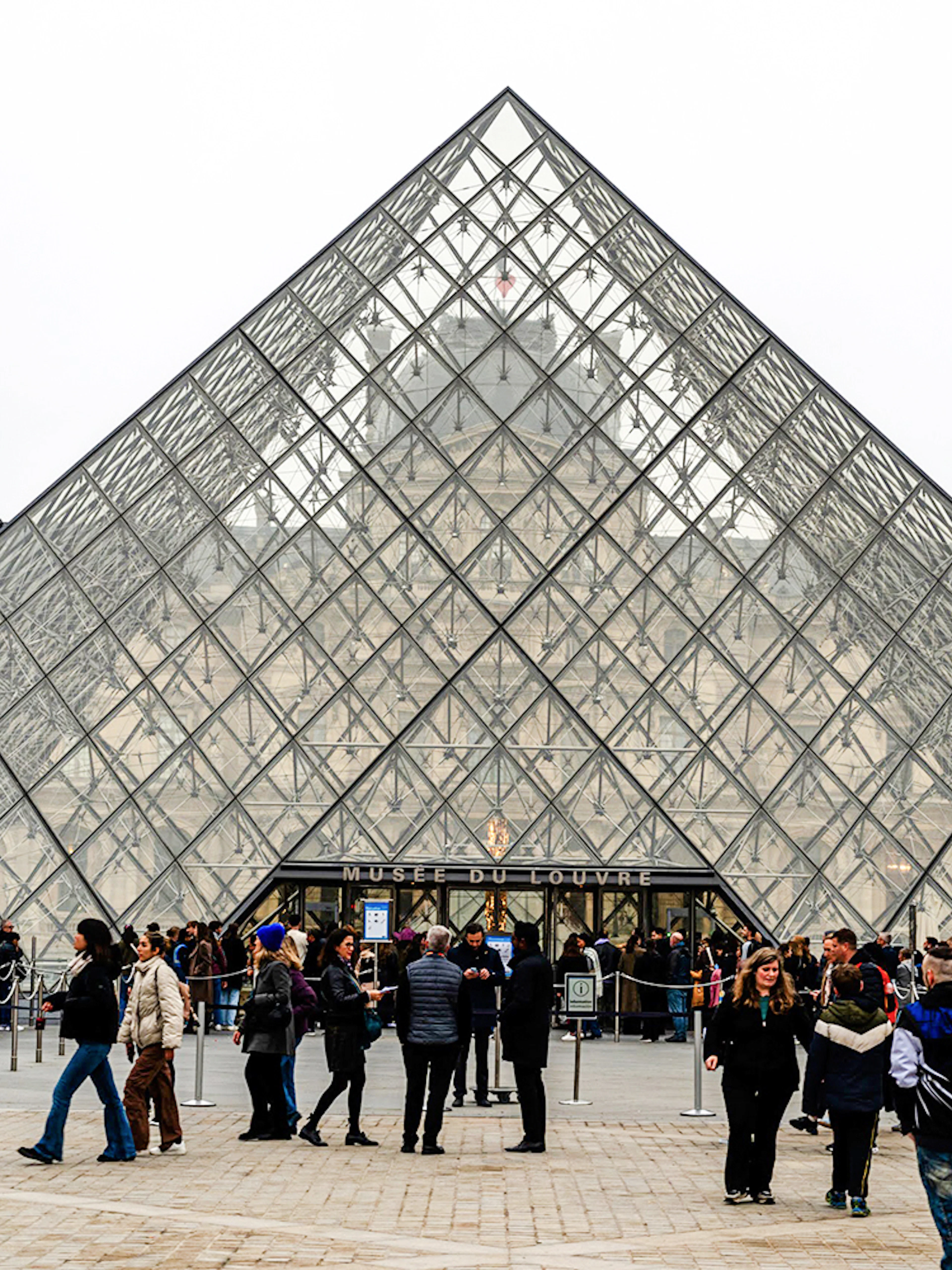 Tourists with guide outside Louvre Museum's glass pyramid entrance, Paris, France.