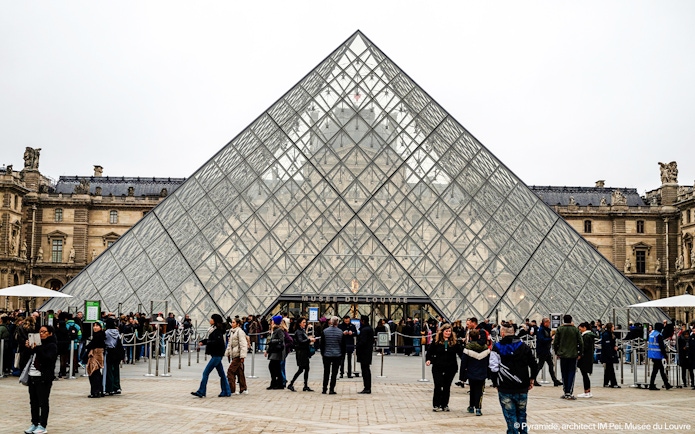 Tourists with guide outside Louvre Museum's glass pyramid entrance, Paris, France.