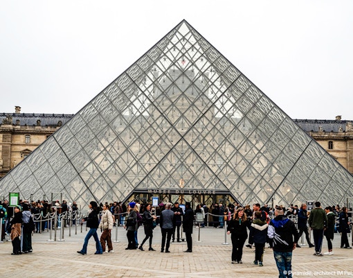 Tourists with guide outside Louvre Museum's glass pyramid entrance, Paris, France.