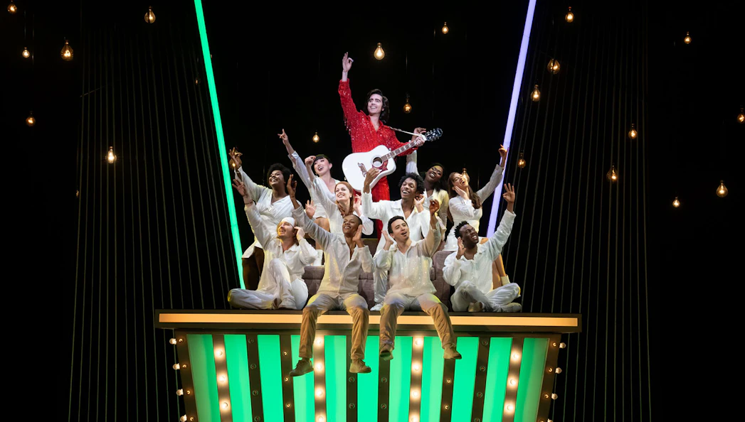 Performers on stage during "A Beautiful Noise: The Neil Diamond Musical" with a guitarist in a red outfit.