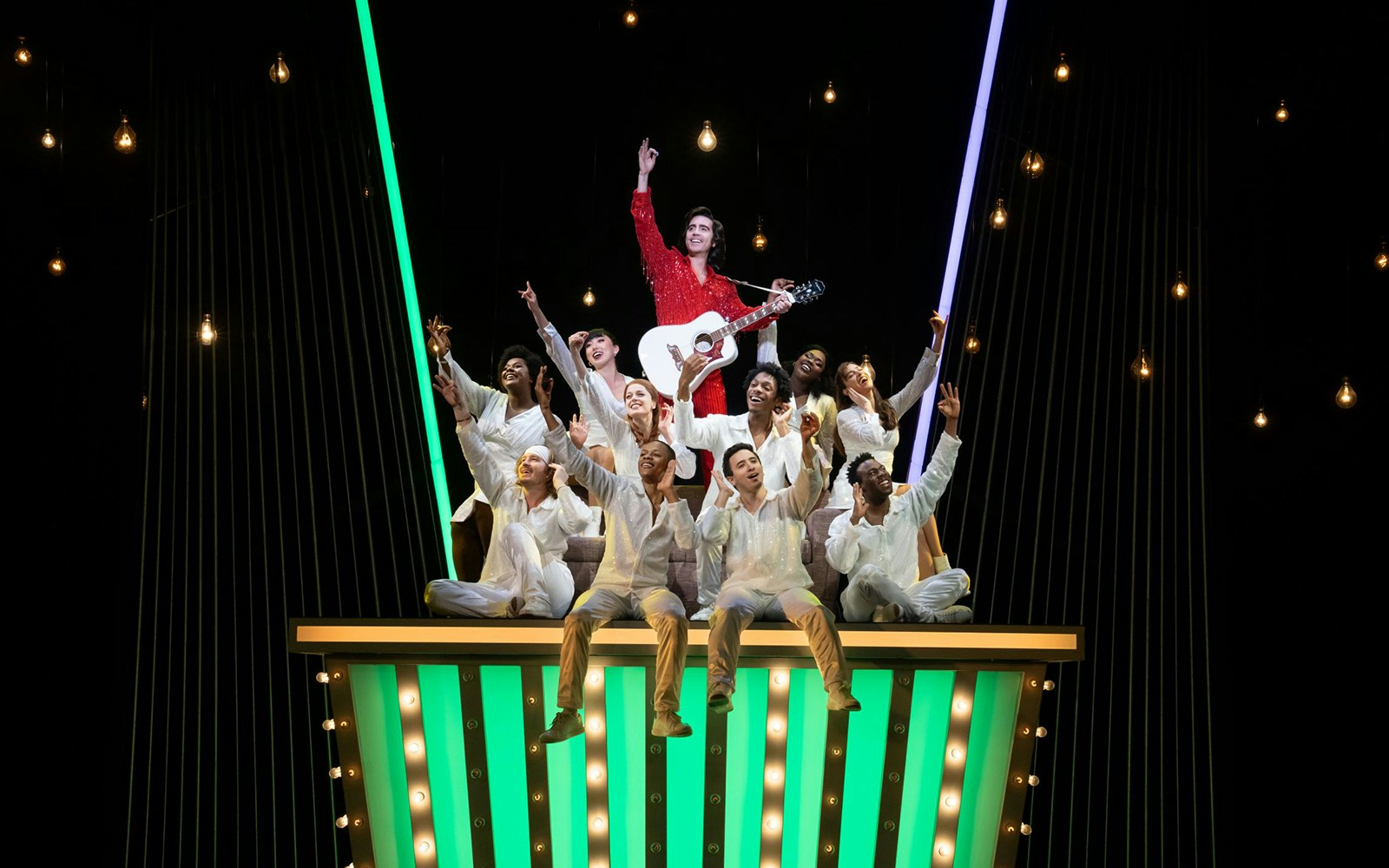 Performers on stage during "A Beautiful Noise: The Neil Diamond Musical" with a guitarist in a red outfit.