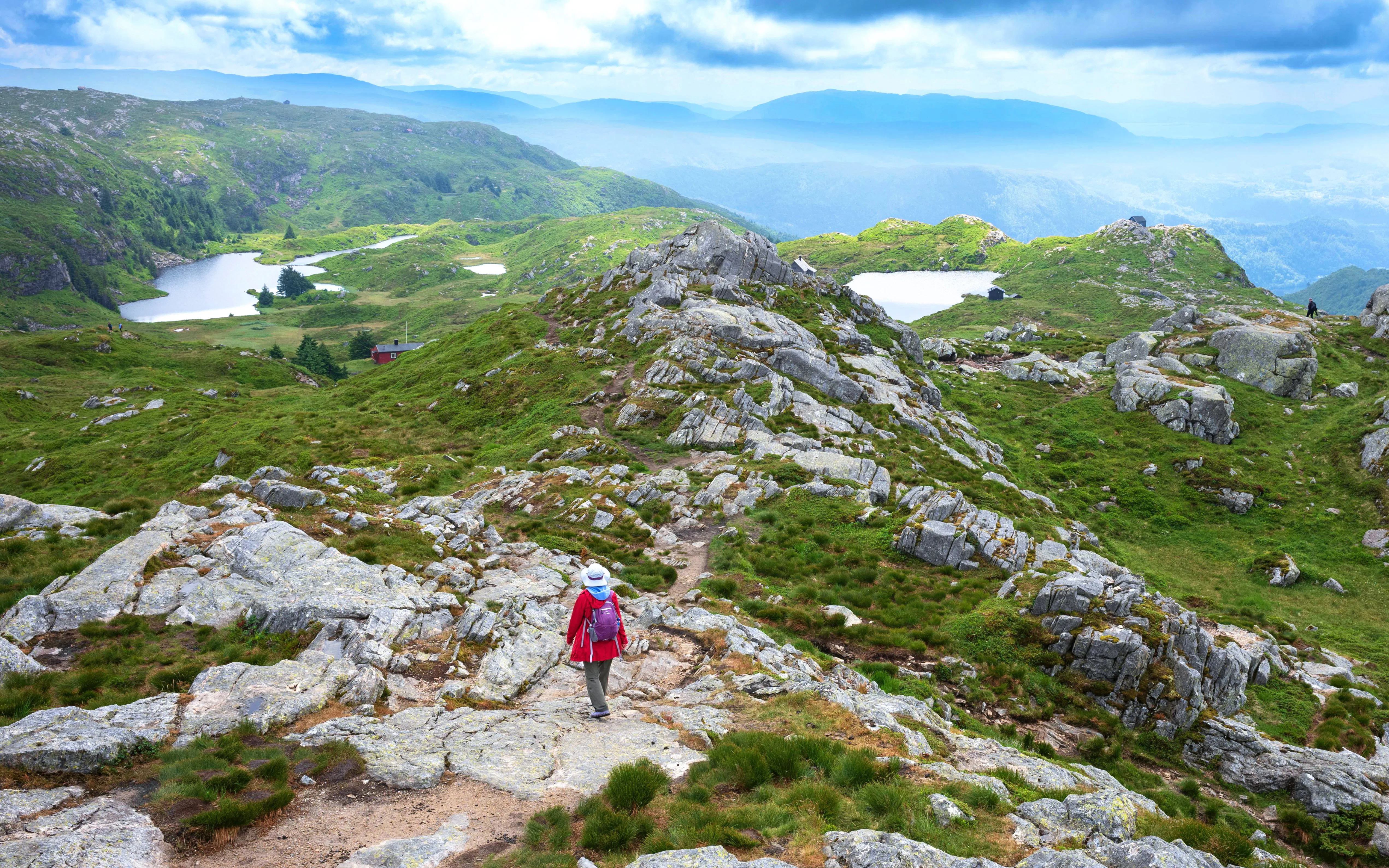 Hiker on rocky trail at the top of Ulriken Mountain near Bergen, Norway, with scenic views.