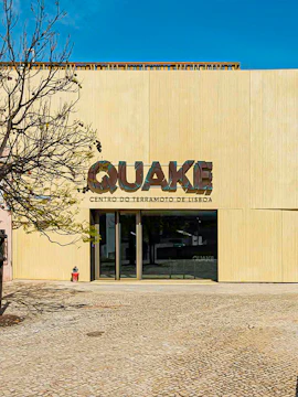 Quake Lisbon Earthquake Centre entrance with tree and cobblestone path.