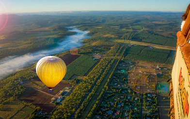 Hot air balloon floating over lush landscape with distant mountains and morning mist.