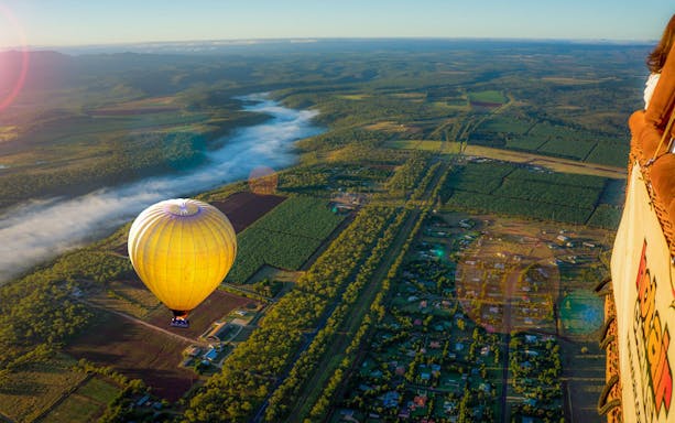 Hot air balloon floating over lush landscape with distant mountains and morning mist.