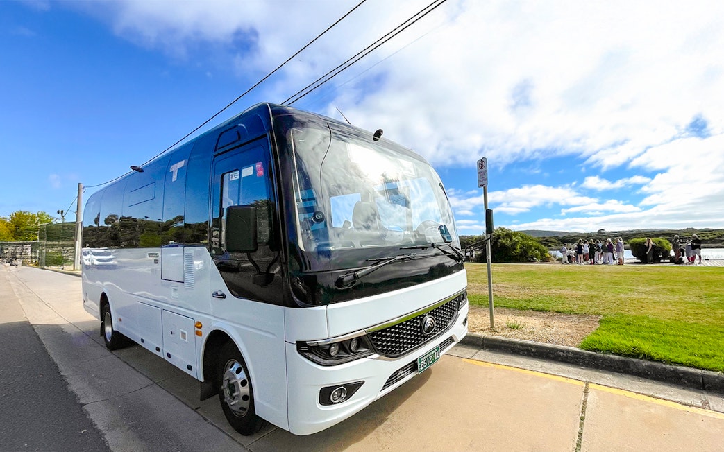 Tour bus parked along Great Ocean Road, Melbourne, with tourists gathering nearby.