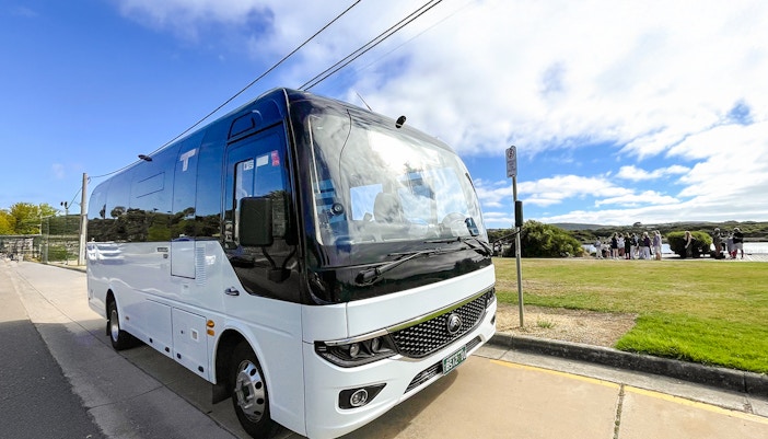 Tour bus parked along Great Ocean Road, Melbourne, with tourists gathering nearby.