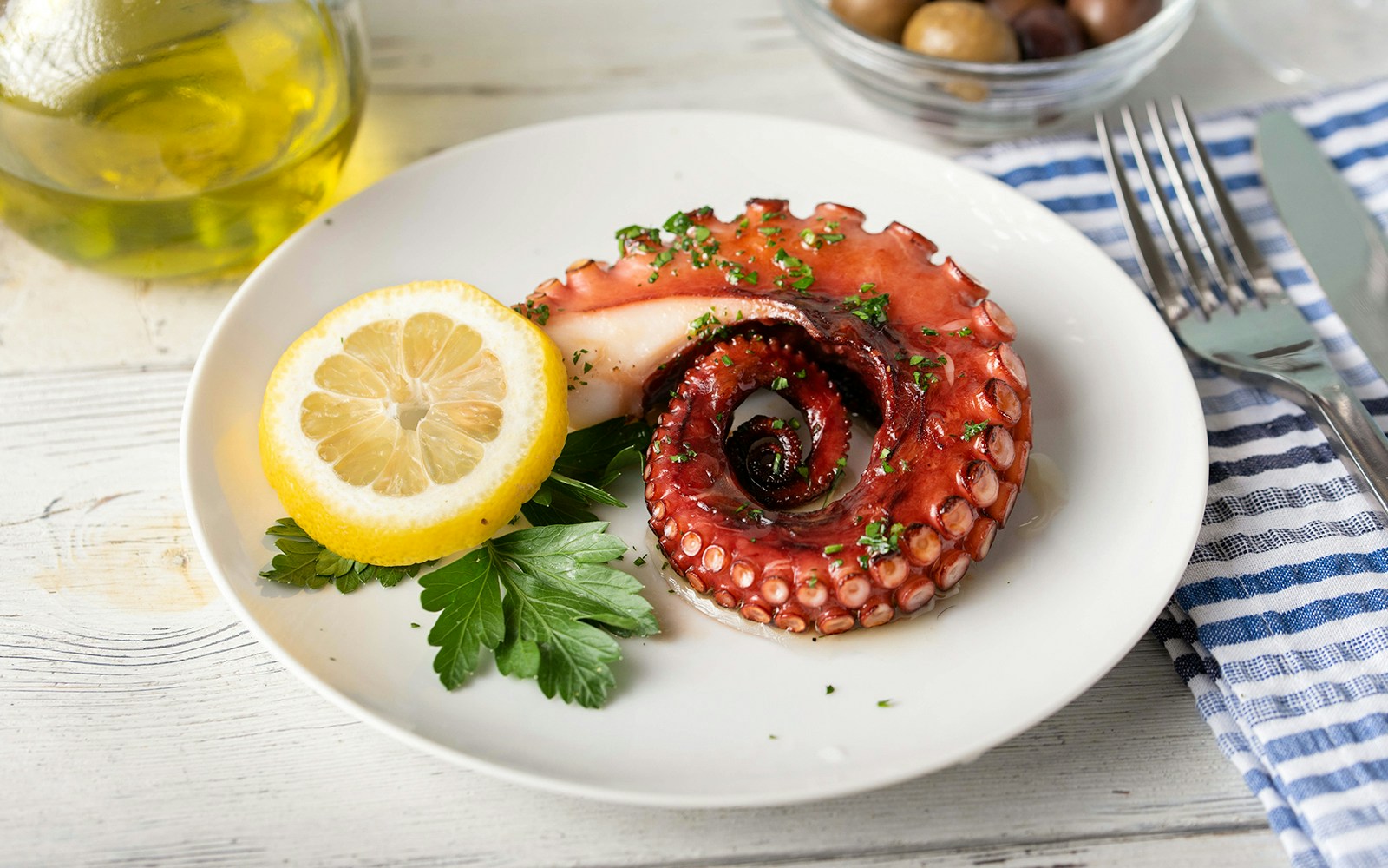 Grilled octopus with lemon and parsley on a white plate, Greek cuisine.