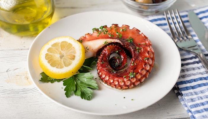 Grilled octopus with lemon and parsley on a white plate, Greek cuisine.
