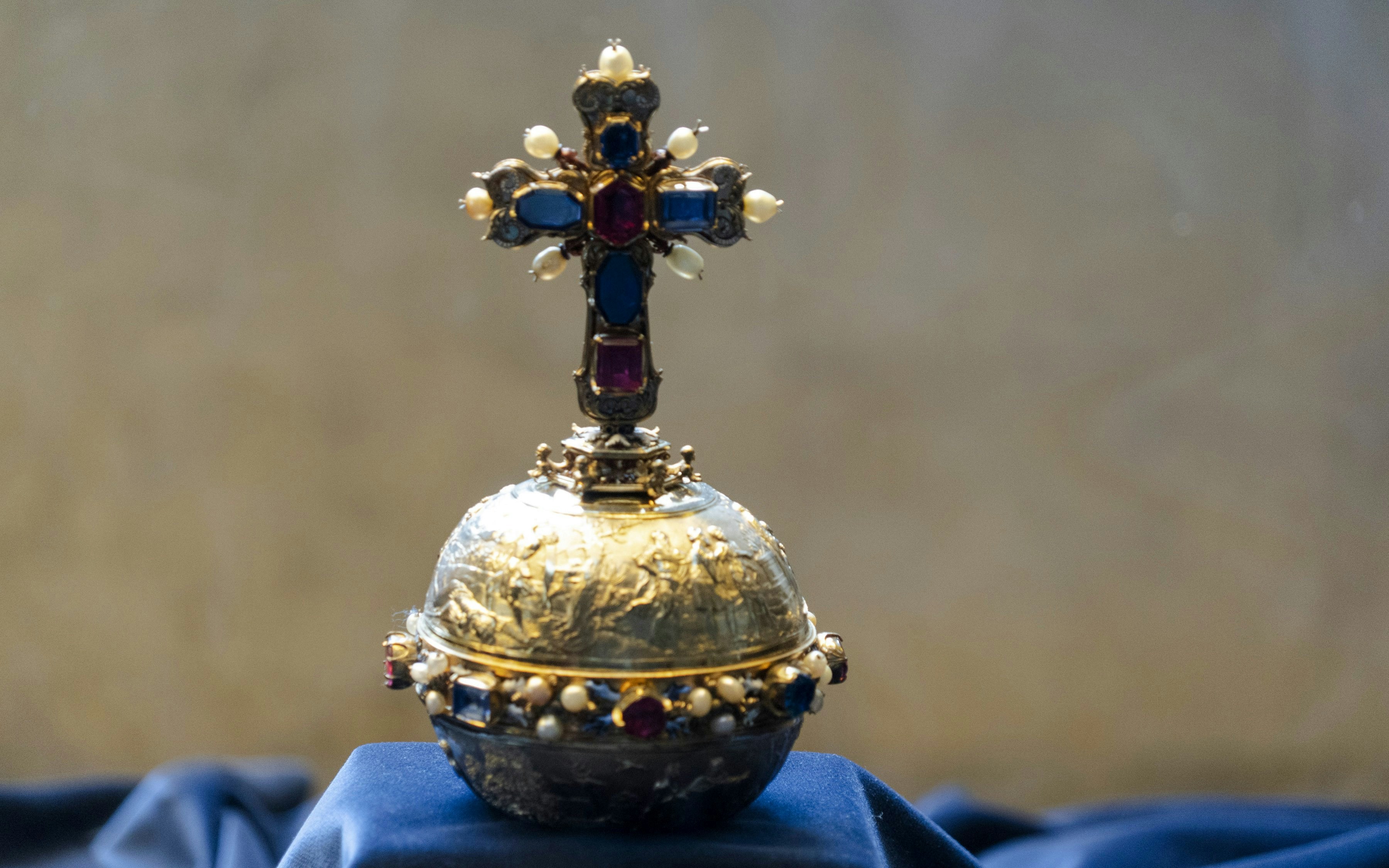 Royal orb adorned with jewels and a cross, displayed on a blue cloth.