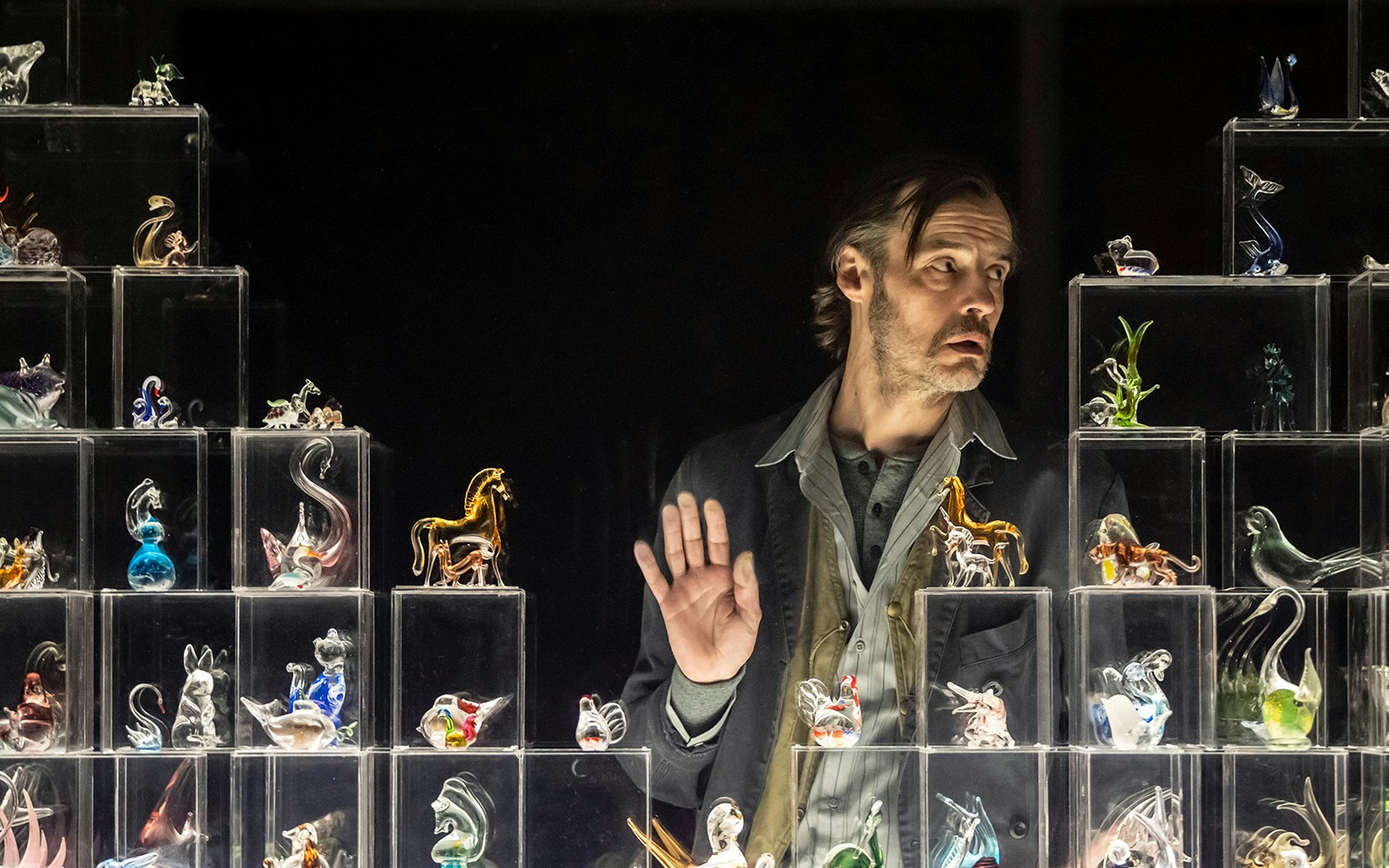 Man observing glass figurines display in "The Glass Menagerie" exhibit.