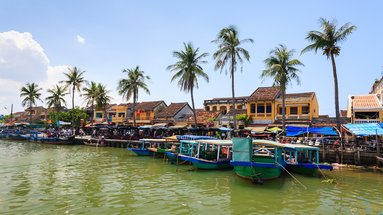 Boats docked at Bach Dang Wharf, Hoi An Ancient Town, with yellow buildings and palm trees.
