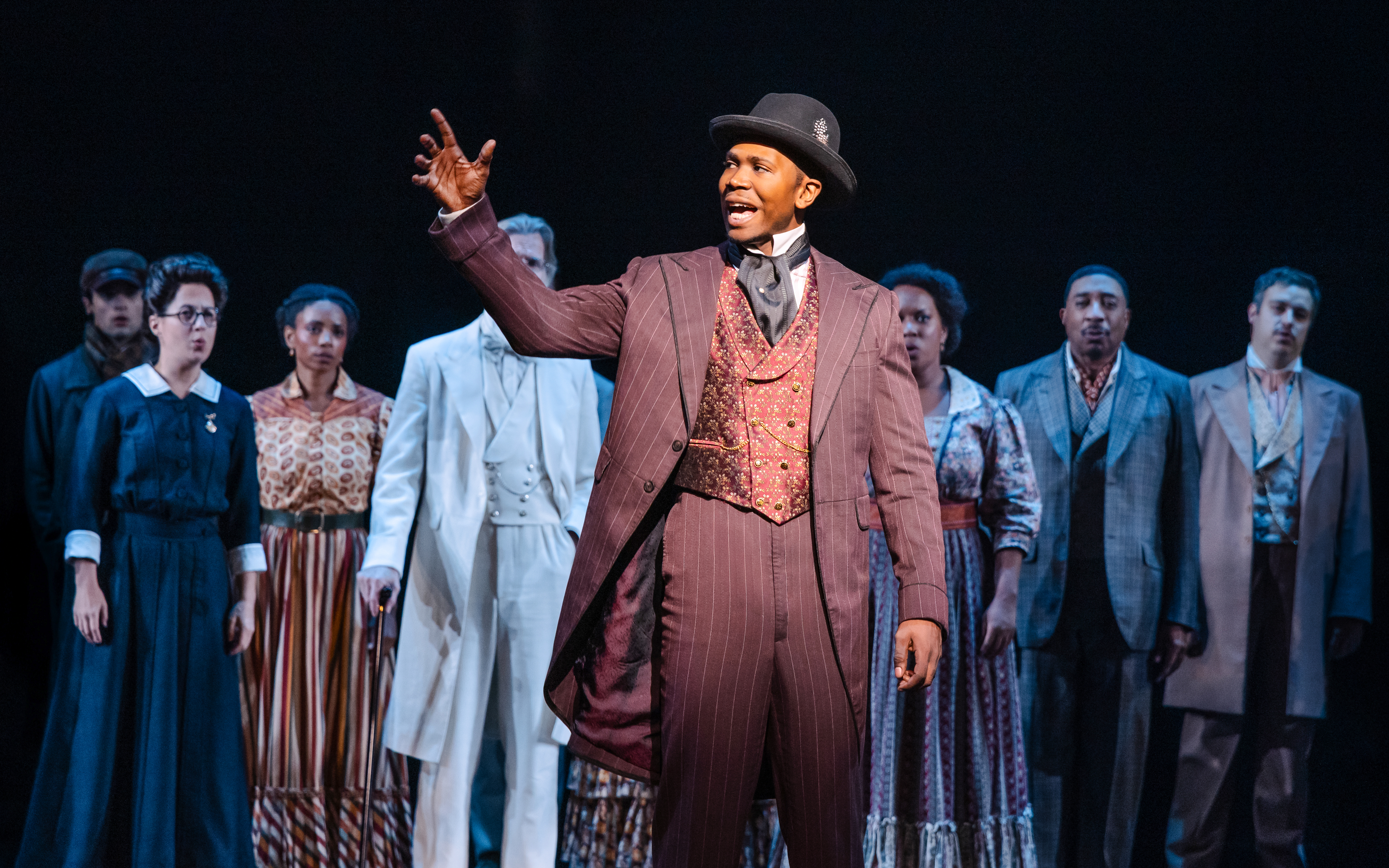 Performer in period costume leading ensemble in Ragtime musical scene.