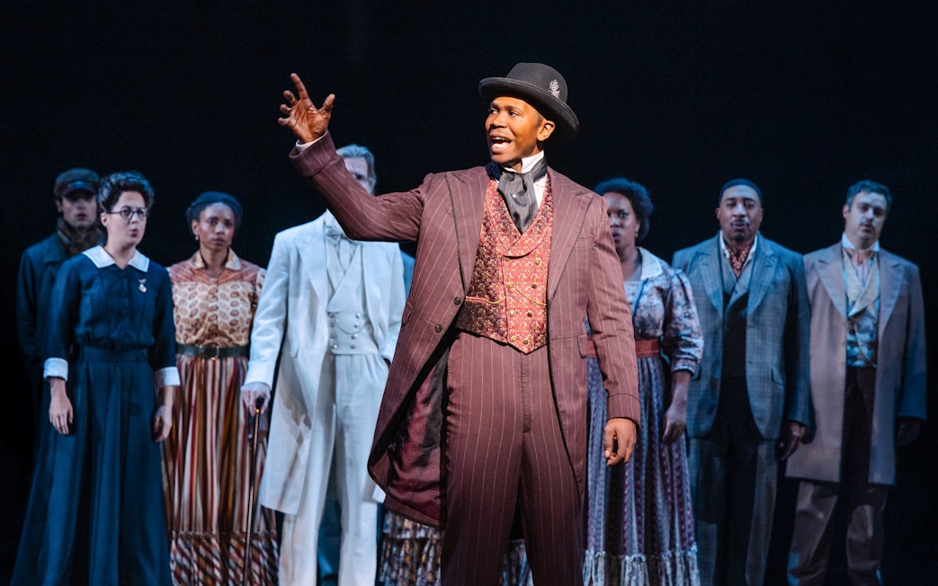 Performer in period costume leading ensemble in Ragtime musical scene.