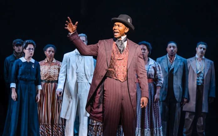 Performer in period costume leading ensemble in Ragtime musical scene.