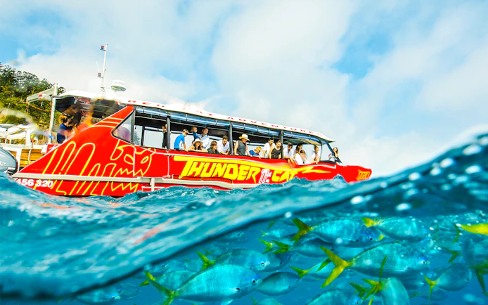 Thundercat boat on Whitsundays tour with tourists, vibrant fish visible underwater.