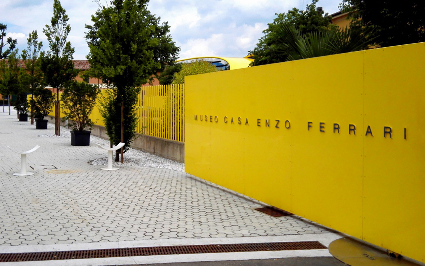 Enzo Ferrari House Museum entrance with yellow wall and trees in Modena, Italy.
